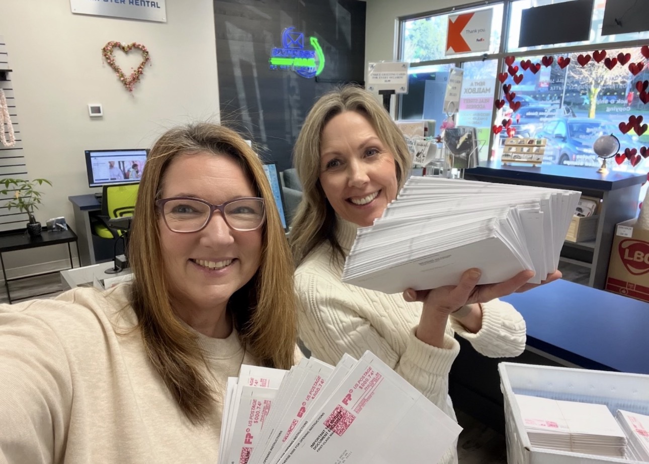 Two women holding stacks of metered mail in the store